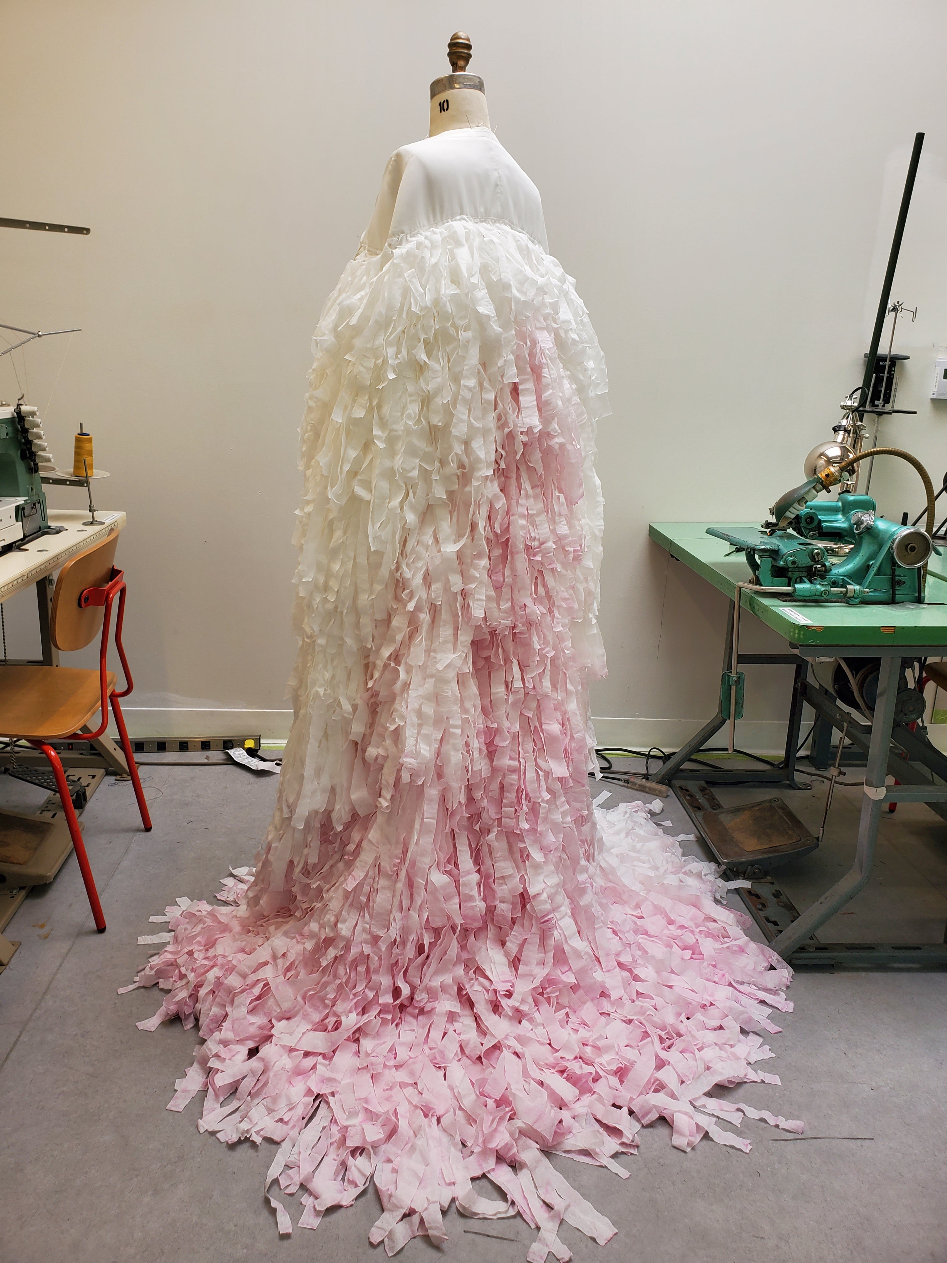 Back profile view of Demascaré's dramatic cape made from multiple strips of Cashmere bathroom tissue in support of the breast cancer cause. 